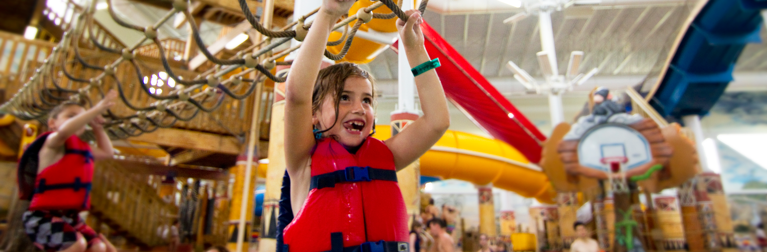 Young girl swinging from monkey bars wearing a life jacket in a water park